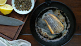 Pan-seared fish fillet in black skillet with lemon halves, capers and chef's knife