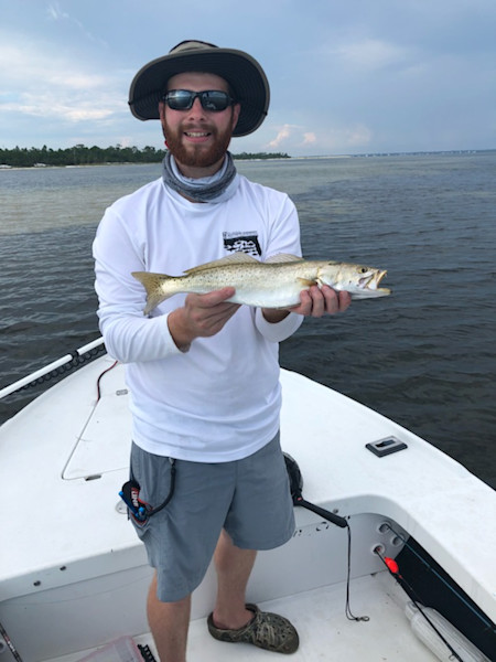 Man holding fish on boat, wearing sun hat, sunglasses, neck gaiter