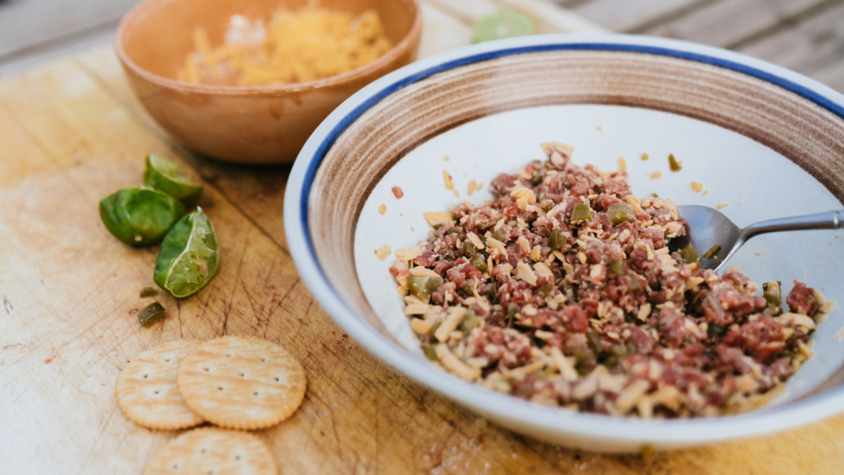 Bowl of chopped meat, cheese, and pickles with crackers and lime wedges