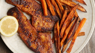 Blackened walleye fillets with sweet potato fries and lemon half on white plate