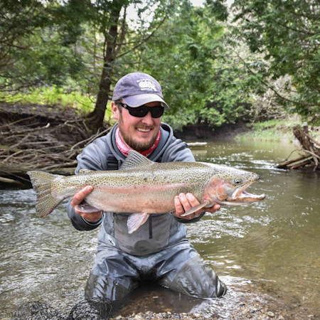 Large rainbow trout held by angler kneeling in a shallow creek