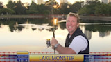 Smiling man holding fishing rod by calm lake at sunrise, on-screen text "LAKE MONSTER"