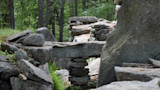 Stacked flat stones forming a small lintel opening among forest boulders
