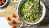 Broccoli tabbouleh with cherry tomatoes in bowl on wooden cutting board