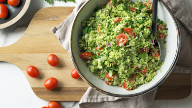 Broccoli tabbouleh with cherry tomatoes in bowl on wooden cutting board