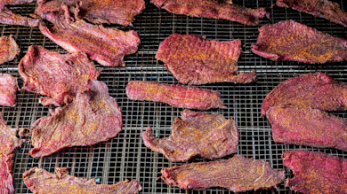 Sliced seasoned jerky drying on metal wire racks