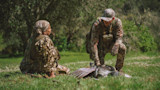 Two hunters in camouflage kneel over a harvested wild turkey in a grassy field