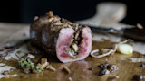 Sliced medium-rare eye-of-round roast stuffed with mushrooms on wooden cutting board, thyme and garlic
