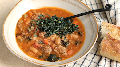 Sausage, bean and kale soup in a bowl with crusty bread and a black spoon