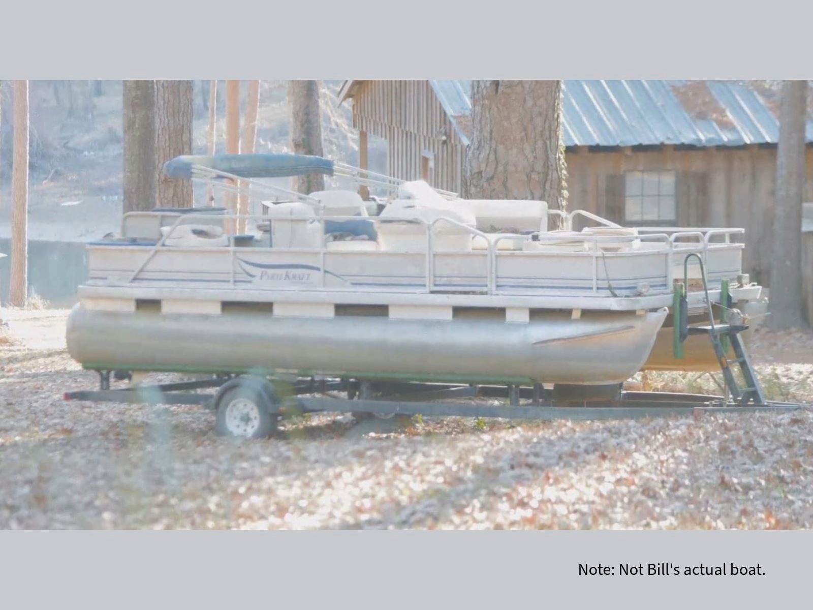 Pontoon boat on trailer parked beside trees and rustic cabin. Note: Not Bill's actual boat.