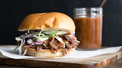 Pulled BBQ sandwich with coleslaw on brioche bun and jar of barbecue sauce