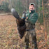 Man in waders holding a beaver by its tail in leaf-strewn woods