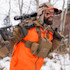 Hunter carrying rifle on shoulder, orange safety vest, camo hood, black face paint, FHF Gear chest pack