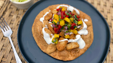 Navajo frybread topped with fried fish, mango salsa and sour cream on dark plate