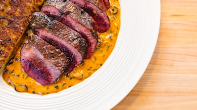 Sliced seared goose breast on creamy pan sauce with potato cake on white plate