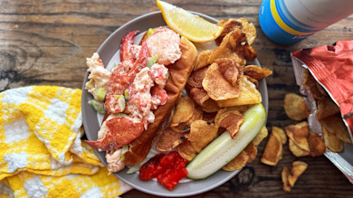 Lobster roll on toasted bun with potato chips, pickle spear and lemon wedge
