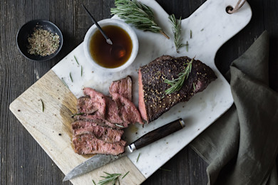 Sous-vide venison roast sliced on marble cutting board with knife, rosemary, and sauce