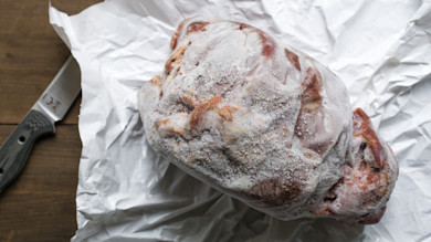 Freezer-burned wild game roast with ice crystals wrapped in mesh on butcher paper, knife beside