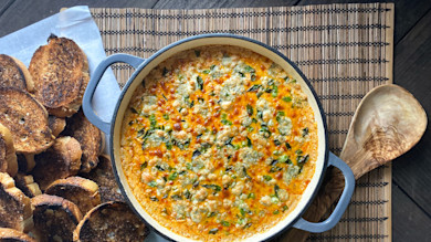 Round pot of cheesy orange dip with blue cheese and scallions; toasted baguette slices