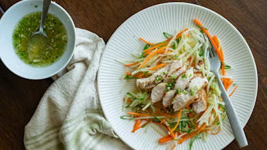 Sliced turkey breast on green papaya and carrot salad, bowl of dressing and fork