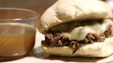 Venison French dip sandwich with melted cheese and a small bowl of au jus