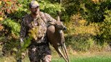 Hunter carrying lifelike doe decoy at field edge near trees