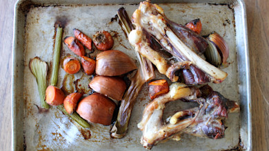 Roasted venison bones with carrots, onions, and celery on a baking sheet