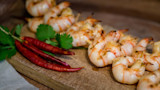 Grilled shrimp skewers on wooden board with red chilies and cilantro