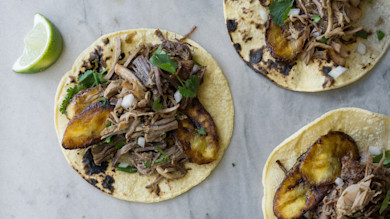 Pork carnitas tacos with fried plantain slices, cilantro and diced onion on corn tortillas, lime wedge