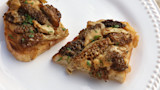 Two toasts on a white plate topped with sauteed morel mushrooms, melted cheese, parsley.