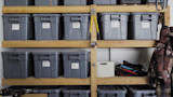 Garage shelves with gray storage bins labeled 'DRY BAGS' and 'DUFFEL BAGS', jackets hanging on right