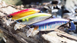 Model Zero fishing lures: three colorful crankbaits on a log by a stream