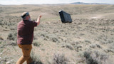 Man tossing hard rifle case across sagebrush in a high desert landscape