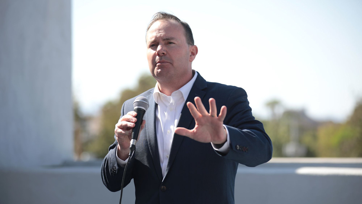 Man in suit speaking into microphone, hand raised outdoors