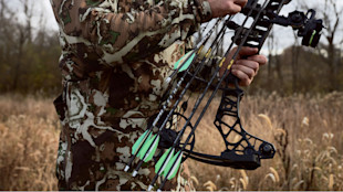 Hunter holding a compound bow and five arrows with bright green fletching