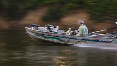 Speeding fishing boat with two men, painted fish on hull, registration "TX 8219 RM"