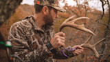 Hunter in camouflage jacket holding elk antlers in autumn forest
