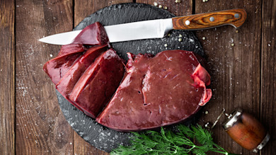 Raw beef liver on round slate with knife, pepper grinder, dill sprigs and coarse salt