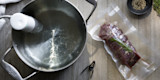 Sous-vide circulator in pot with vacuum-sealed meat and rosemary in FoodSaver bag