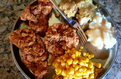 Fried chicken, corn, mashed potatoes with gravy and stuffing on metal plate