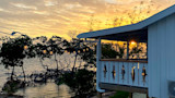 Sunset over mangrove shoreline with string lights and a lodge porch featuring fish cutouts