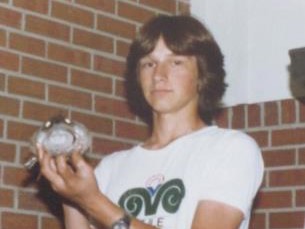 Teen holding small round object toward camera, standing by brick wall