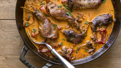 Braised rabbit legs in creamy tomato and pepper sauce, garnished with parsley, in cast-iron skillet with spoon