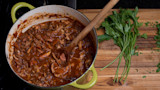 Rabbit ragu in green Dutch oven with wooden spoon and parsley on a cutting board