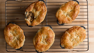 Six golden-brown pot pies on a cooling rack, one cut open revealing savory filling