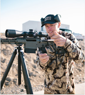 Man adjusting rifle with SIG Sauer scope mounted on tripod