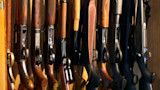 Assorted rifles and shotguns lined upright inside a wooden gun cabinet