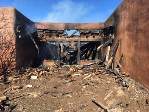 Charred, collapsed adobe house with burned roof and smoldering debris