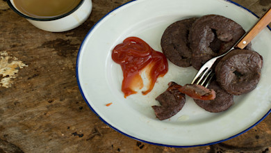 Fried venison heart slices with ketchup on an enamel plate, fork and coffee mug on wooden table