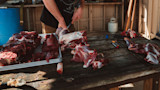 Butchered venison on wooden table as a person carves meat; T-shirt reads 'MEATEATER'